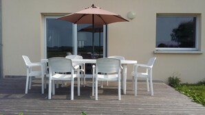 Een terras met een tafel, stoelen, parasol en een raam.