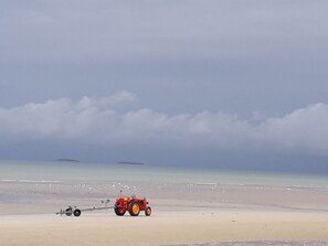 A red tractor on a sandy beach with a calm sea and overcast sky in the background.