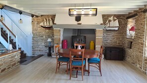 A dining area with a wooden table and chairs, a stone wall, a staircase, and a wood-burning stove. - BRETONNE LONGERE BETWEEN SEA AND COUNTRYSIDE (Plouhinec)