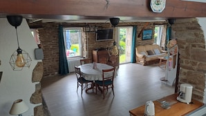 A rustic room with a stone wall, wooden floor, a round table with chairs, a sofa, and a coffee table with a kettle. - BRETONNE LONGERE BETWEEN SEA AND COUNTRYSIDE (Plouhinec)