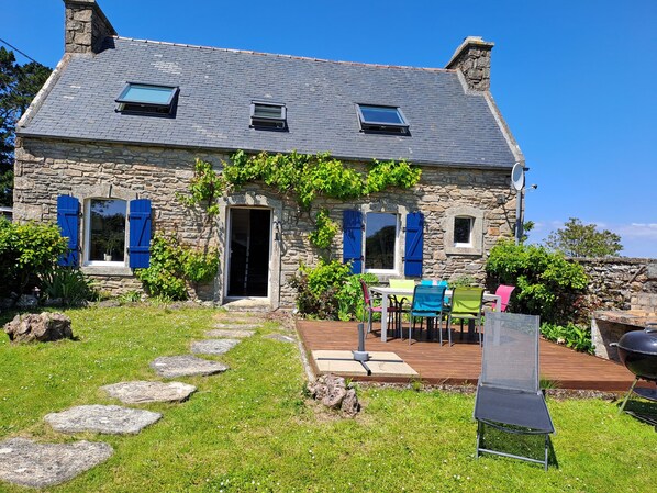 A stone house with a sloped roof, a wooden deck, and a stone pathway leading to the entrance.