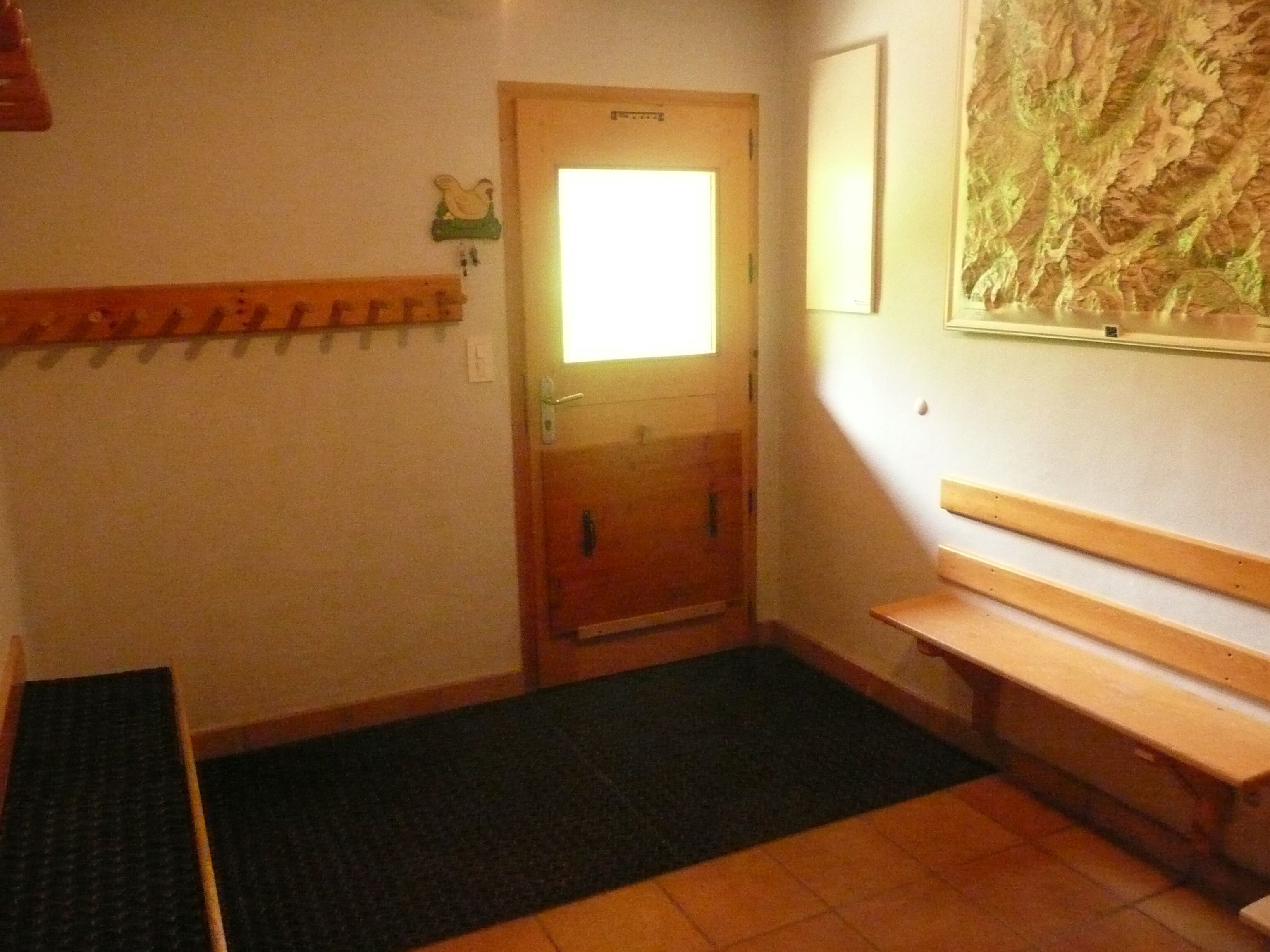 Un pasillo con un banco de madera, una puerta con ventanal y un perchero en la pared.