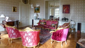 A room with a large, ornate sofa set, a piano, and a mirror. - Château de la Voûte, facing south (Troo)