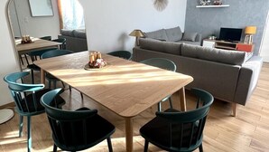 Een moderne woonkamer met een houten eettafel, donkergroene stoelen, een grijze bank en een hanglamp.