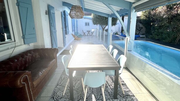 Een overdekt terras met eethoek en een zwembad.