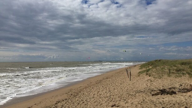 Een strand met een zandstrand, een grasduin en een bewolkte lucht.