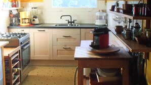Een kleine keuken met een gasfornuis, gootsteen en diverse apparaten. Er is een raam dat natuurlijk licht en uitzicht op groen biedt.