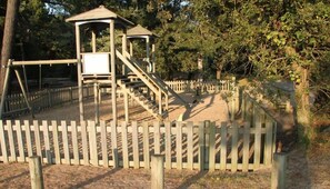 Un parque infantil con valla de madera, estructura para escalar y zona de arena.