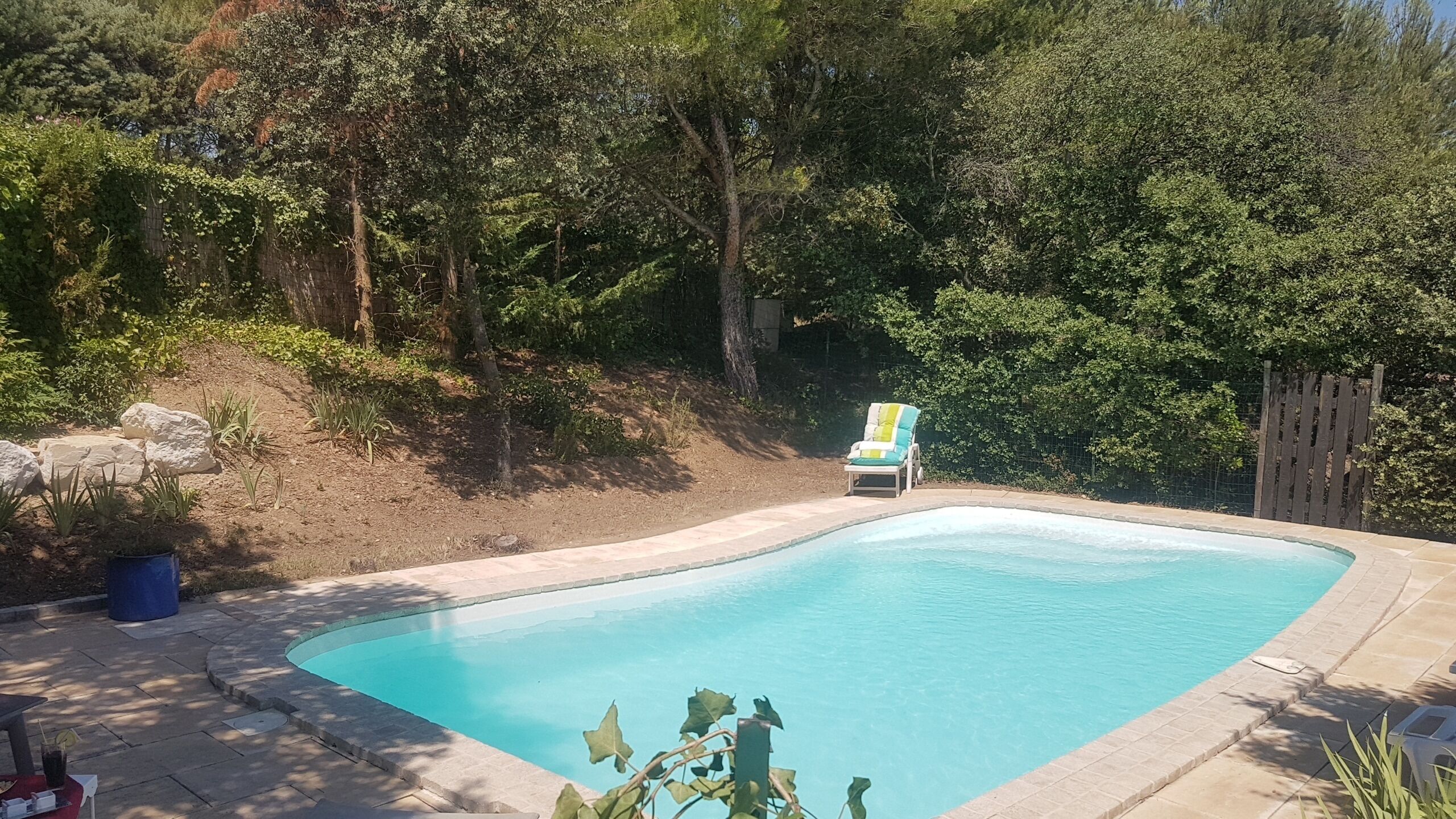 Una piscina amb vora corba, envoltada per un solàrium de pedra. Hi ha una cadira relaxant i una taula petita amb una beguda.