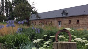A rustic brick building with a sloped roof, surrounded by a garden with various plants and flowers.