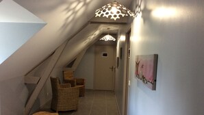 A narrow hallway with a sloped ceiling, wicker furniture, and a door at the end.