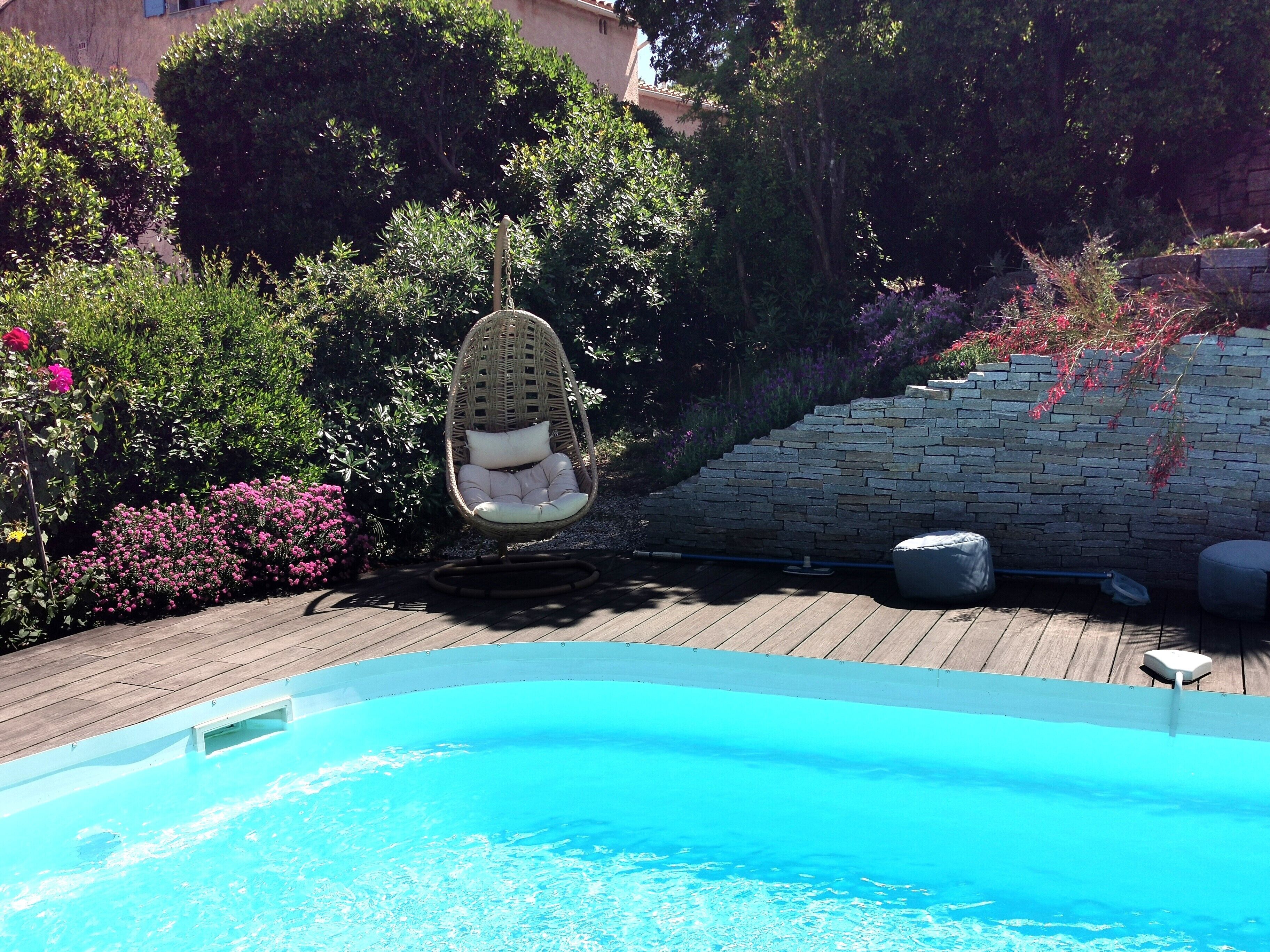 A pool area with a hanging chair, a stone wall, and lush greenery.