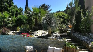 An outdoor patio with a stone wall, a pool, and a seating area with wooden furniture. - Superb sea-view villa with landscaped pool. Large garden, for 1 or 2 families (Cavalaire-Sur-Mer)