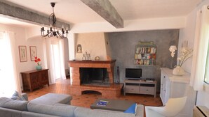 A living room with a fireplace, a sofa, a television, and a bookshelf. - Superb sea-view villa with landscaped pool. Large garden, for 1 or 2 families (Cavalaire-Sur-Mer)