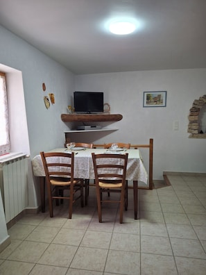 A dining area with a table set for two, a television above the table, and a decorative brick arch on the wall. - GIte in a quiet hamlet near Gordes (Gordes)