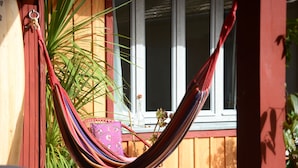 A hammock tied between a wooden structure and a window, with a potted plant and a window in the background. - Superb seaside villa, warm and fully equipped (Vieux-Boucau-Les-Bains)