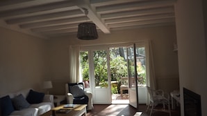 A living room with a white sofa, a wooden coffee table, and a patterned rug. There is a glass door leading to an outdoor area with a patio and a chair. - Superb seaside villa, warm and fully equipped (Vieux-Boucau-Les-Bains)