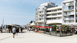 A coastal promenade with multi-story buildings, outdoor seating, and a clear sky.