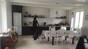 Una cocina moderna con una isla central, un comedor con mesa y sillas, y una persona de pie junto al mostrador.