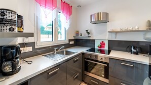 A modern kitchen with stainless steel appliances, a double sink, and a window with red curtains.