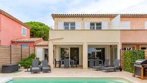 A two-story house with a swimming pool, outdoor seating, and a barbecue area.