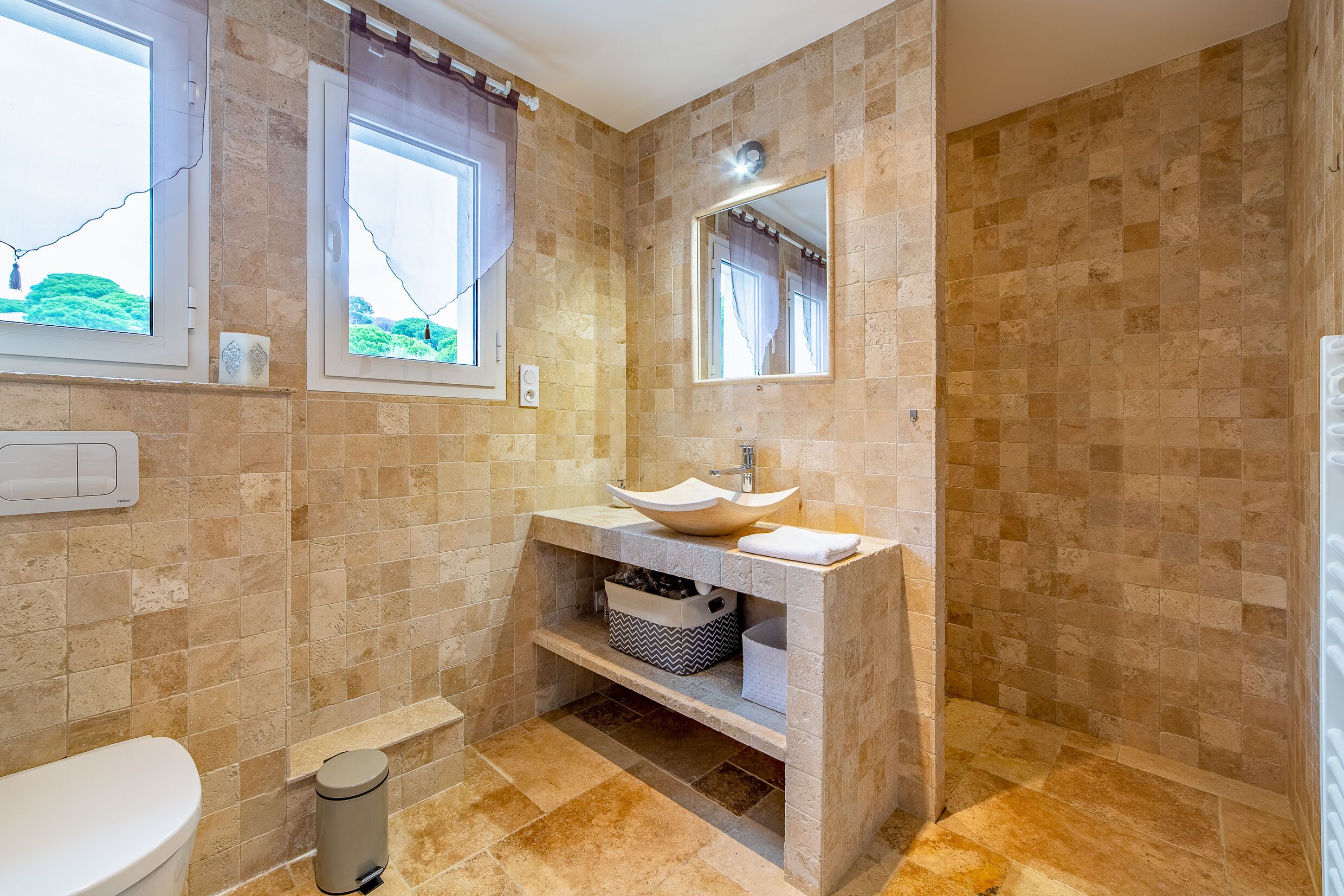 A bathroom with beige tiles, a white sink, a mirror, and a window with curtains.