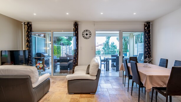 A modern living room with a sofa, a dining table with chairs, a TV, and a large window with curtains.