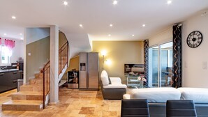 A spacious living area with a staircase, a kitchen, a dining area, and a bedroom with a large bed and a TV.