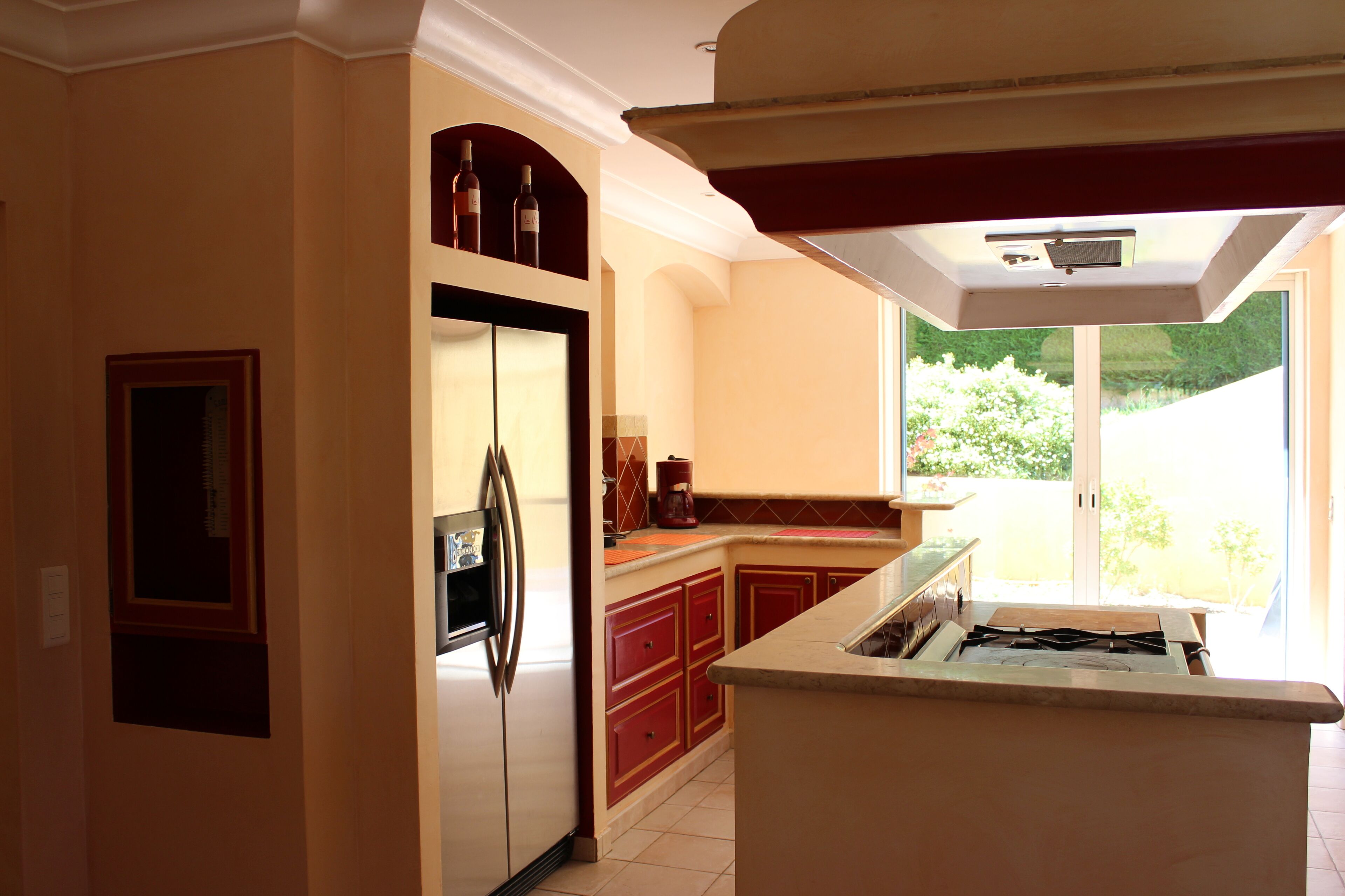 Una cocina con refrigerador integrado, gabinetes rojos, estufa a gas y ventana con vista a un jardín.