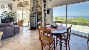 Ein gemütliches Wohnzimmer mit Kamin aus Naturstein, ein Essbereich mit Meerblick und ein großes Fenster.