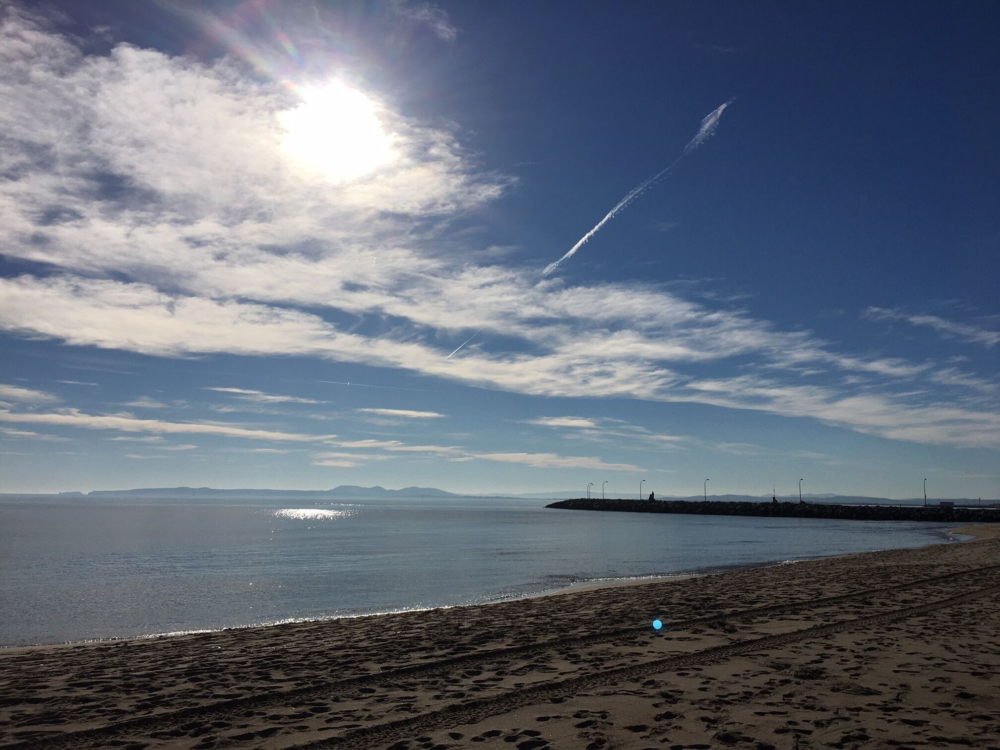 A beach with footprints leading to the water, a clear sky, and distant mountains.