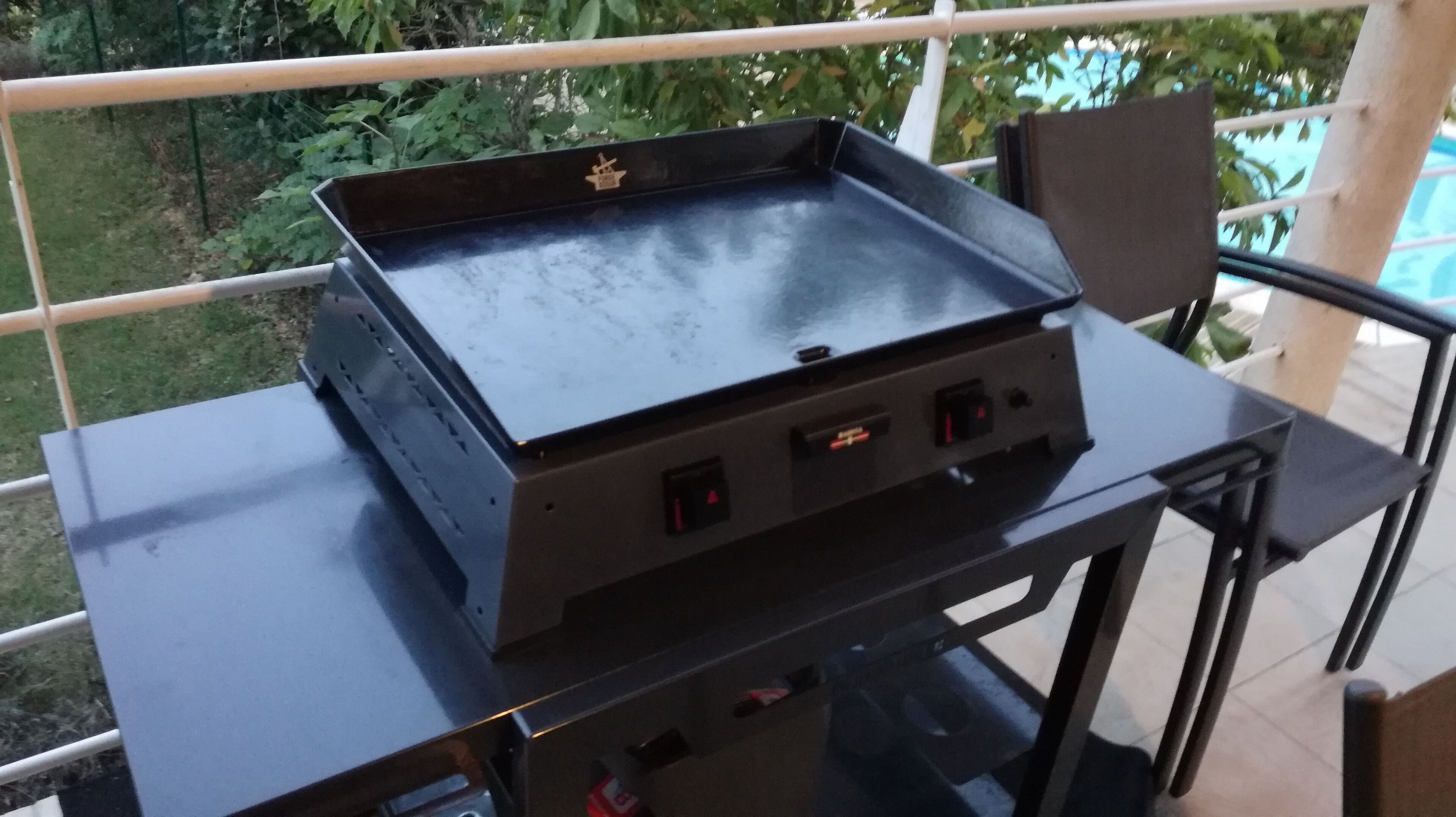 A portable grill on an outdoor table with a railing in the background.