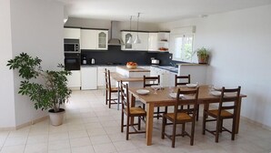 A modern kitchen with white cabinets, a central island, and a dining area with wooden chairs and a table. - GITE NEAR CAHORS WITH PRIVATE HEATED POOL (Le Montat)