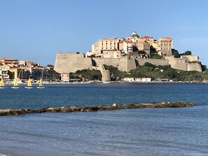 A coastal cityscape with a prominent castle-like structure on a hill, overlooking a calm sea with several sailboats. - T3 4P terrace garage air conditioning wifi beach and shops 2 mn away  (Calvi)
