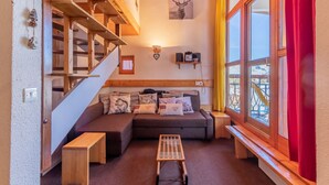 Une pièce chaleureuse avec un escalier en bois, un canapé agrémenté de coussins décoratifs, une petite table et un tableau représentant un cerf, accroché au mur.