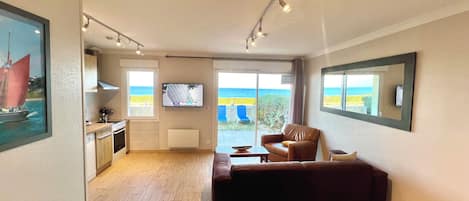 A modern living room with a sofa, a television, and a view of the sea through large windows.