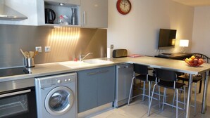 Pieni, käytännöllinen keittiö, jossa on pyykinpesukone, leivänpaahdin ja hedelmäkulho työtasolla.