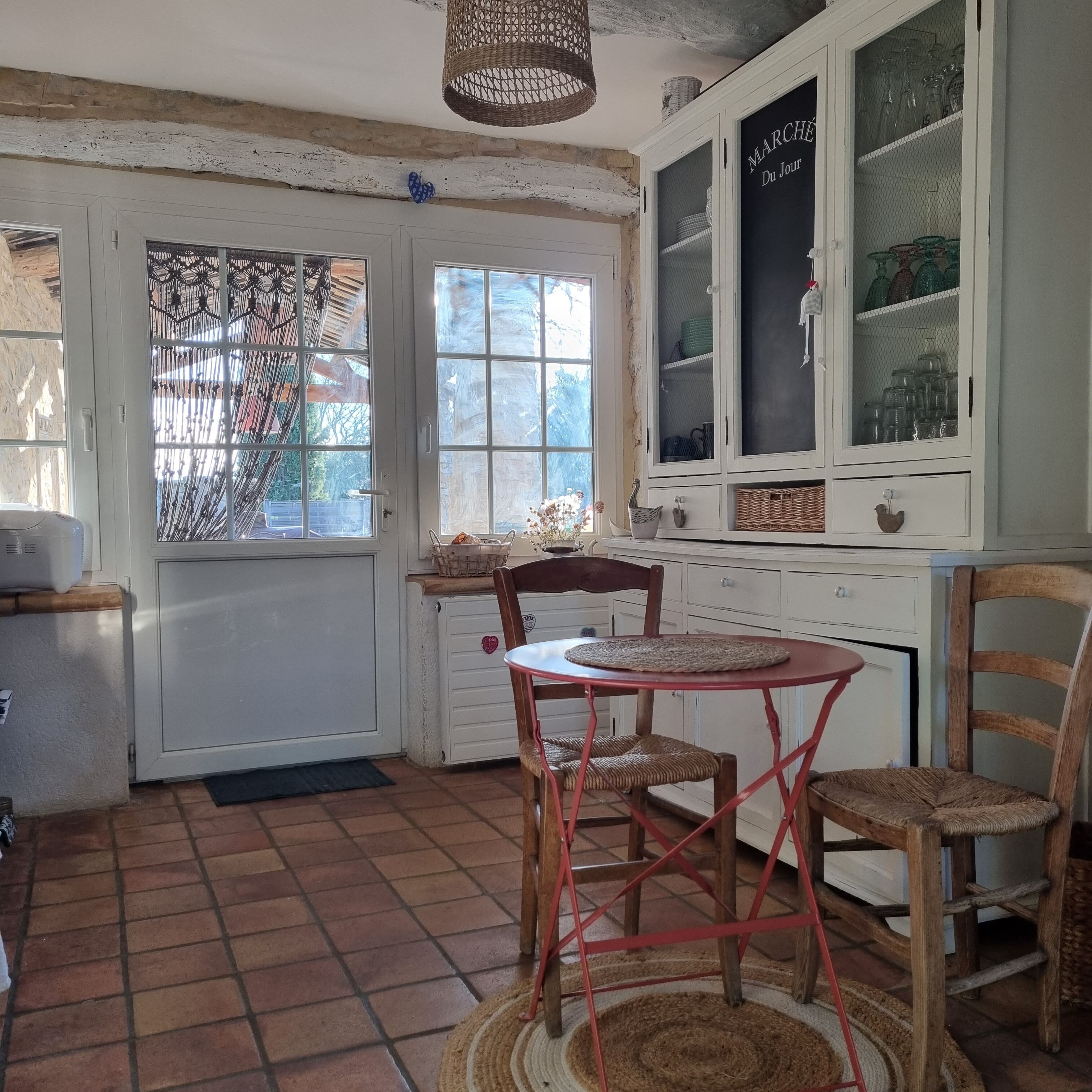 Une cuisine rustique avec un sol carrelé, une table ronde entourée de chaises et un buffet aux portes vitrées.