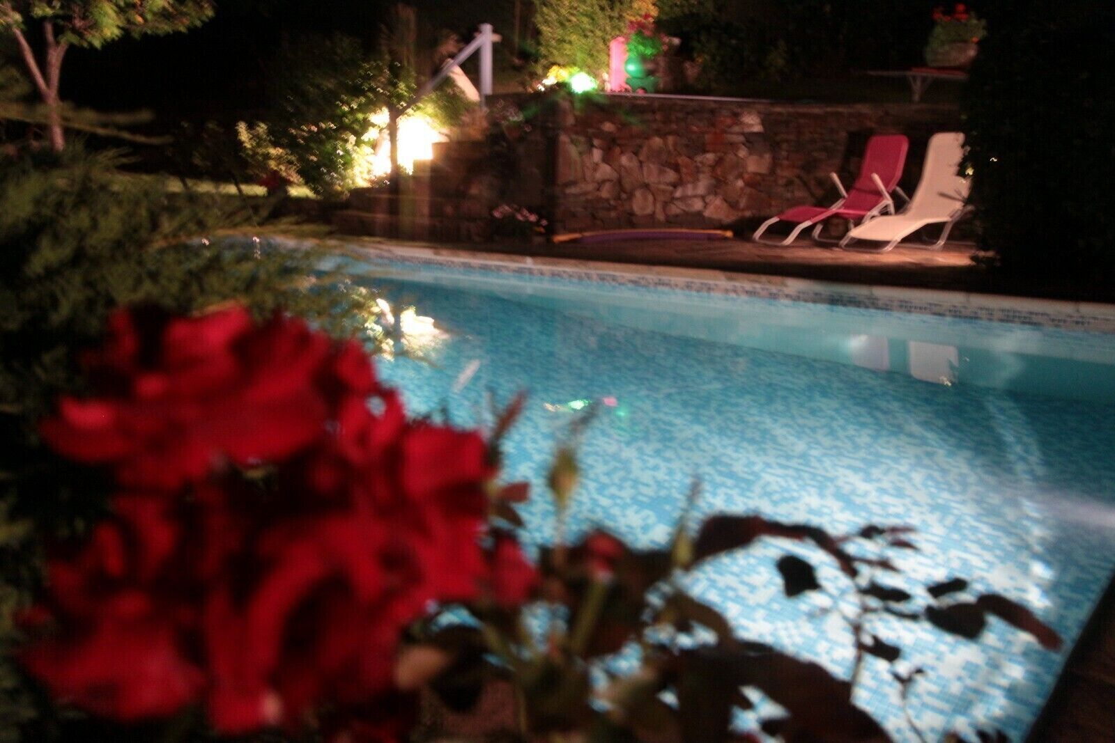 A swimming pool with a stone wall and lounge chairs.