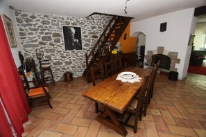 Un espace repas comprenant une table en bois, des chaises, un mur en pierre, un escalier et une cheminée.