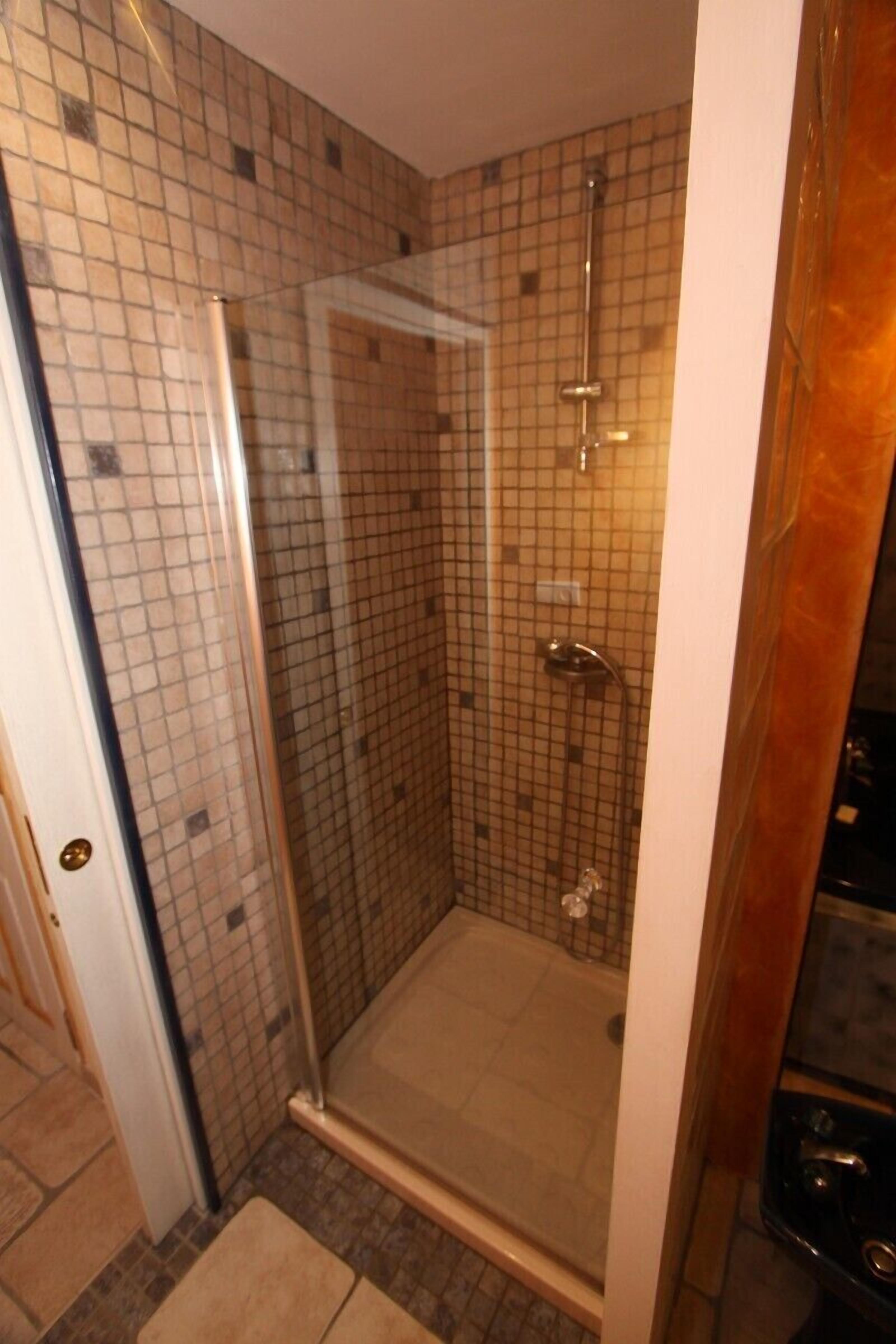 A glass-enclosed shower with a tiled wall and a door leading to another room.