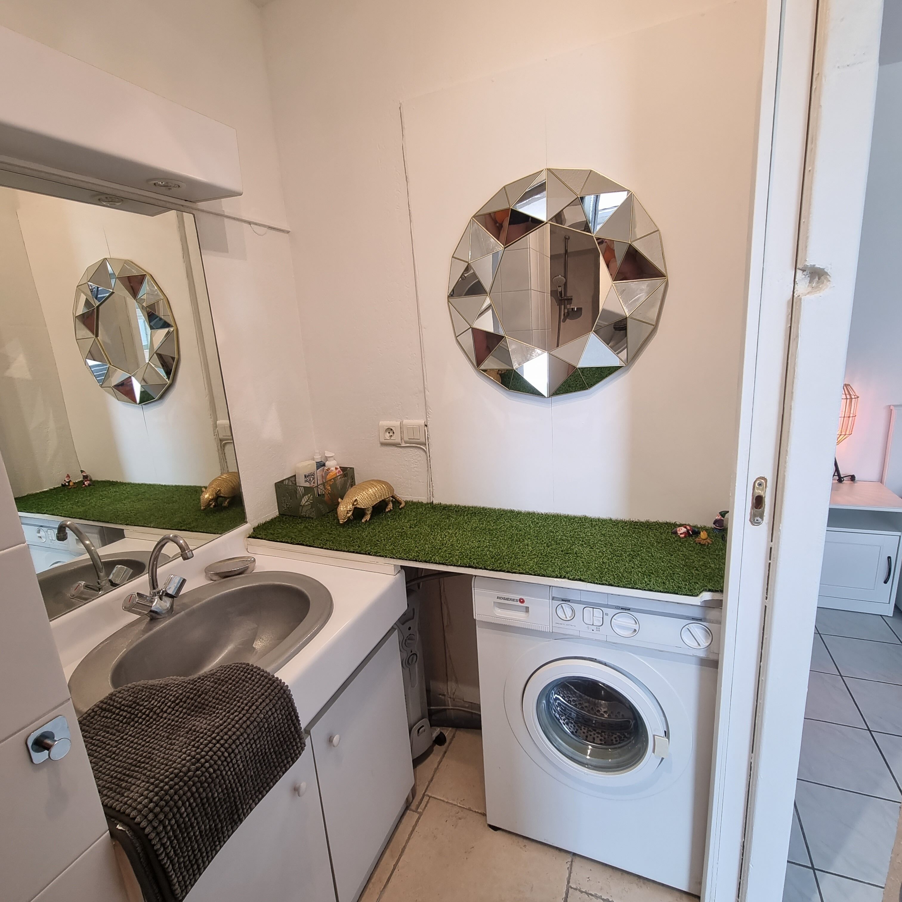 A compact kitchen with a sink, a washing machine, and a mirror with a geometric design.