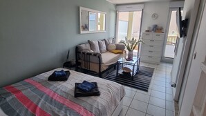 A bedroom with a bed, a sofa, a small table, a mirror, and a view of the outside. -  PRETTY STUDIO quiet, well located for the beaches of St Raphael and Frejus (Fréjus)