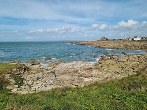 A coastal landscape with rocky terrain, a clear sky, and a few buildings in the distance. - TY PRAT- Vacation rental in PENMARCH / from 2 to 6 people (Penmarch)