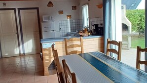 Un'ampia sala da pranzo con un lungo tavolo e sedie, una cucina sullo sfondo e vista sull'esterno.