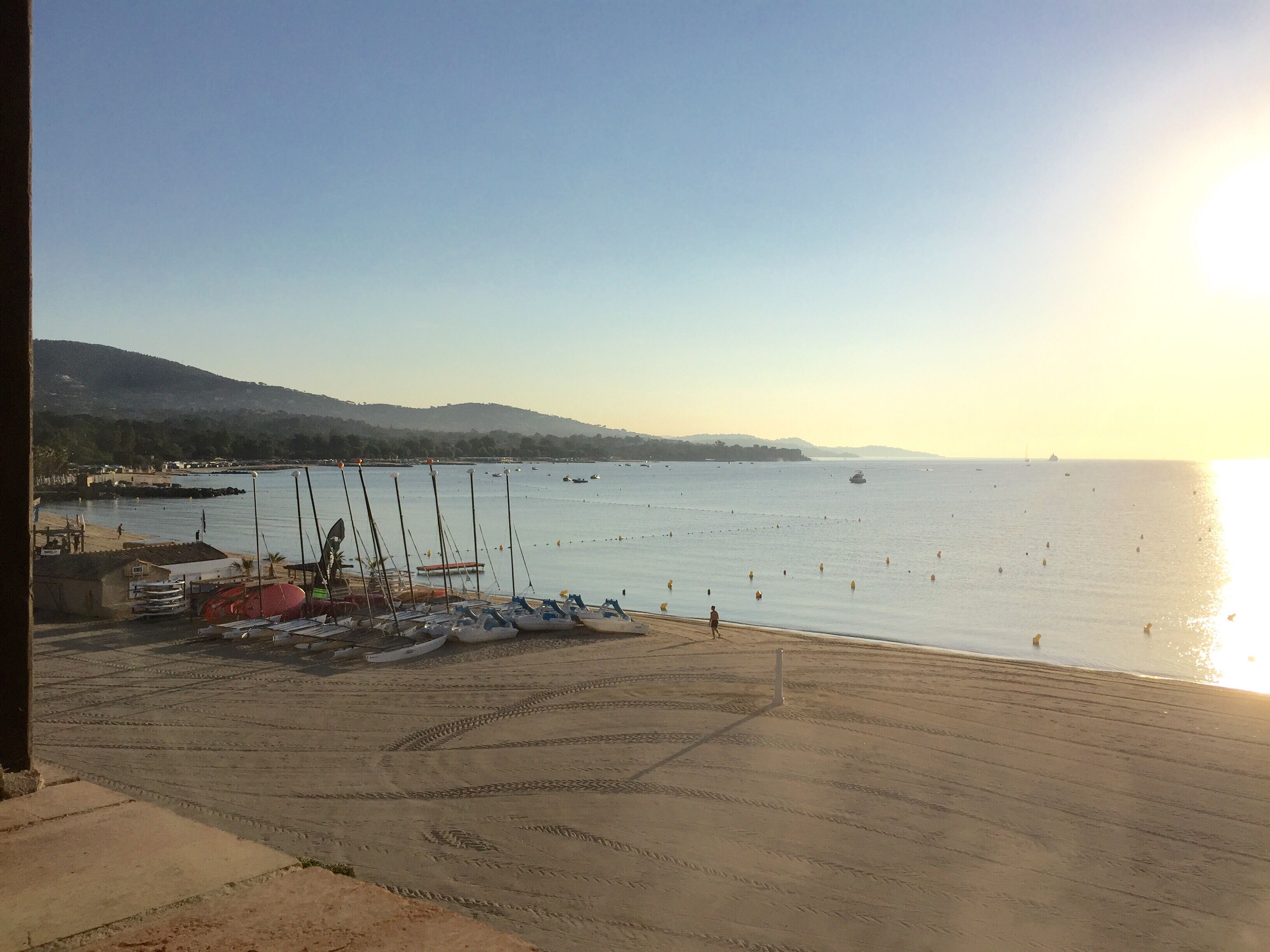 A beachside view with boats docked, a sandy area, and a calm sea.