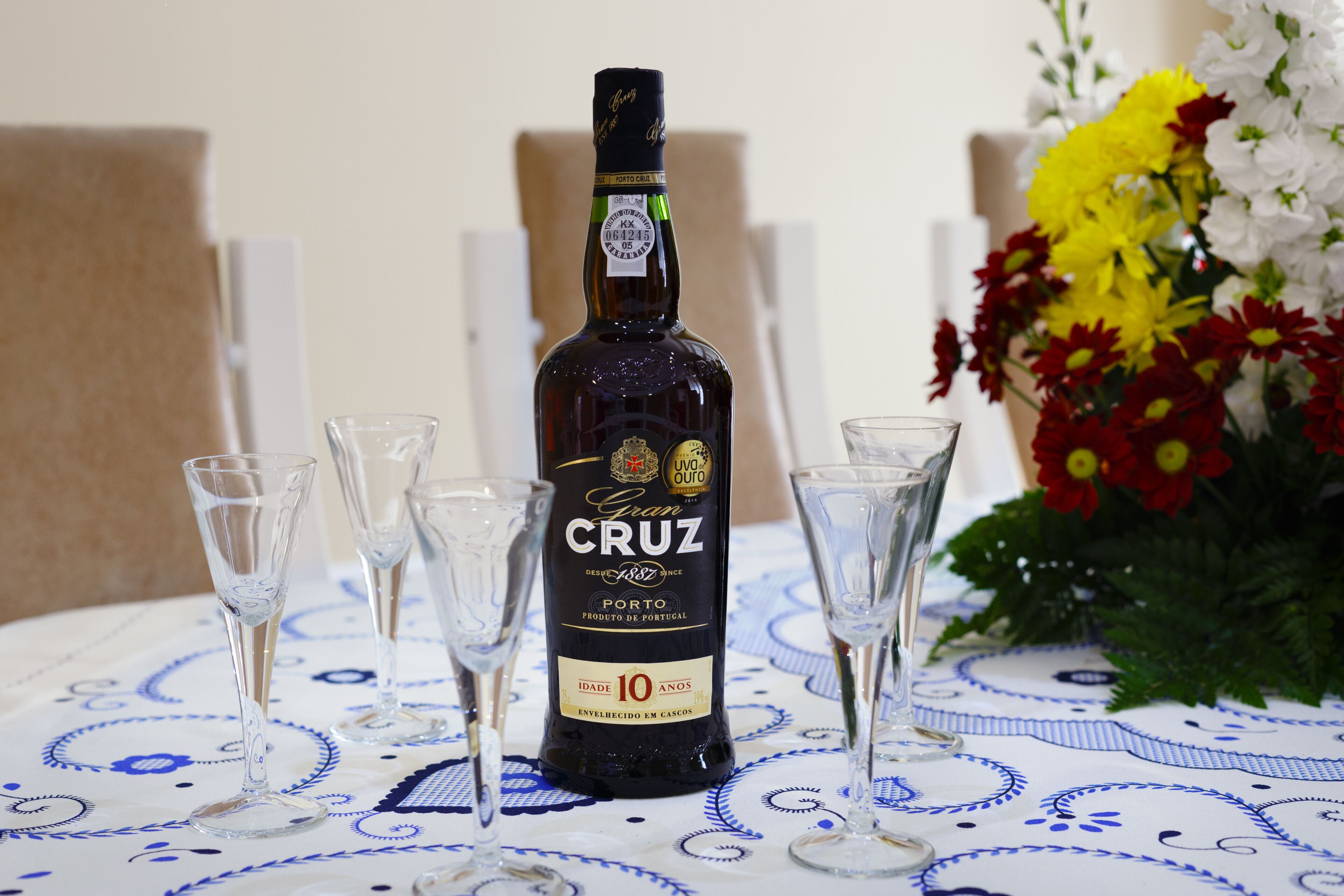 Eine Flasche Cruz Porto Wein mit einem Etikett, das angibt, dass es sich um ein 10 Jahre altes Produkt handelt, umgeben von vier leeren Weingläsern auf einem Tisch mit einer blau-weißen Tischdecke.