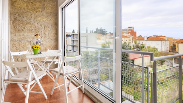 A balcony with a white table and chairs, a potted plant, and a view of buildings and greenery. - Very nice apartment in the center of Porto (Oporto)