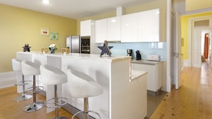 A modern kitchen with white cabinets, a marble island with bar stools, stainless steel appliances, and a wooden star decoration. - Very nice apartment in the center of Porto (Oporto)