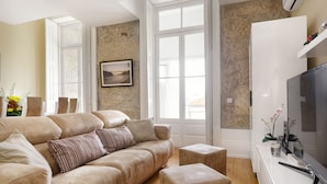 A living room with a beige sofa, a coffee table, and a flat-screen TV on a white stand. - Very nice apartment in the center of Porto (Oporto)